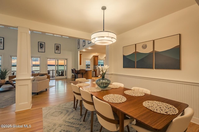 dining room featuring light wood-type flooring, ornate columns, and a wainscoted wall