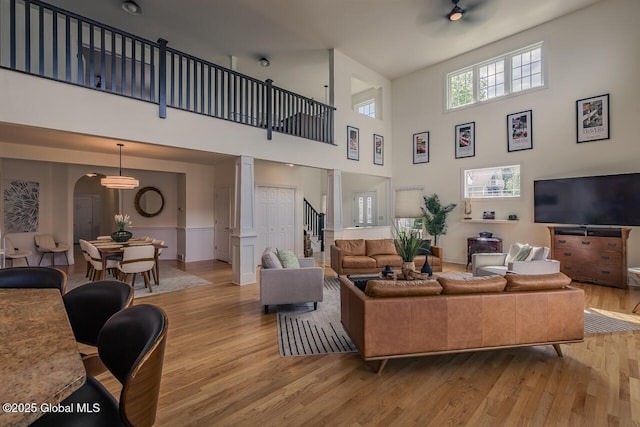 living area featuring light wood-style floors, arched walkways, a high ceiling, and ornate columns