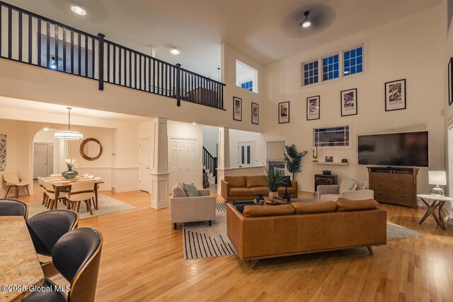 living area with arched walkways, a high ceiling, light wood-type flooring, and stairs