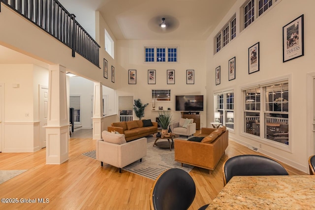 living room with light wood-type flooring, wainscoting, decorative columns, and a towering ceiling