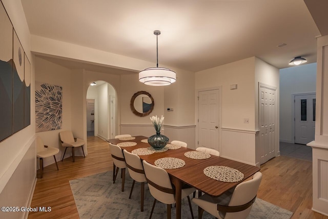 dining area featuring light wood-style floors, arched walkways, and wainscoting