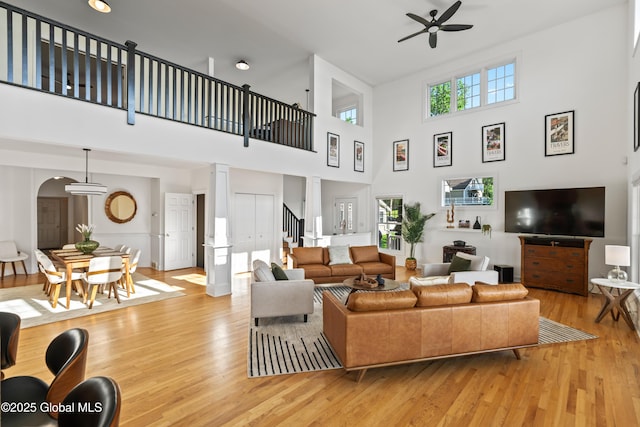 living room with arched walkways, ornate columns, light wood-style flooring, and a ceiling fan