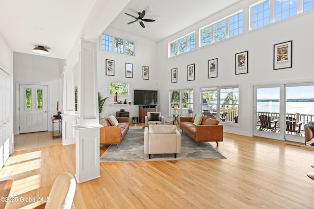 living area with ornate columns, a high ceiling, a ceiling fan, and light wood-style floors