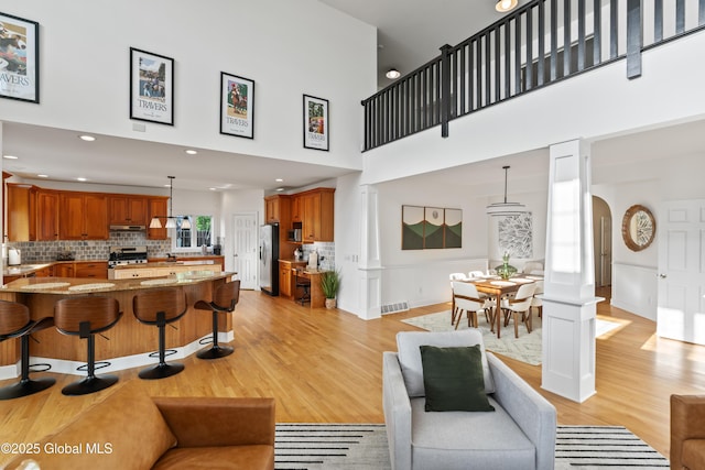 living area featuring arched walkways, light wood-style flooring, a high ceiling, and visible vents