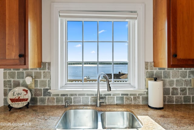 kitchen featuring tasteful backsplash, brown cabinetry, a water view, and a sink