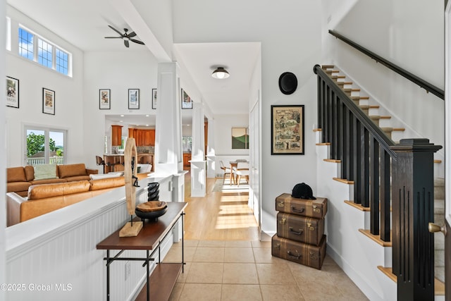 entryway featuring light tile patterned flooring, a towering ceiling, baseboards, a ceiling fan, and stairway