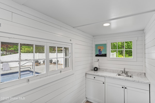 kitchen featuring light stone counters, white cabinets, a sink, and wood walls