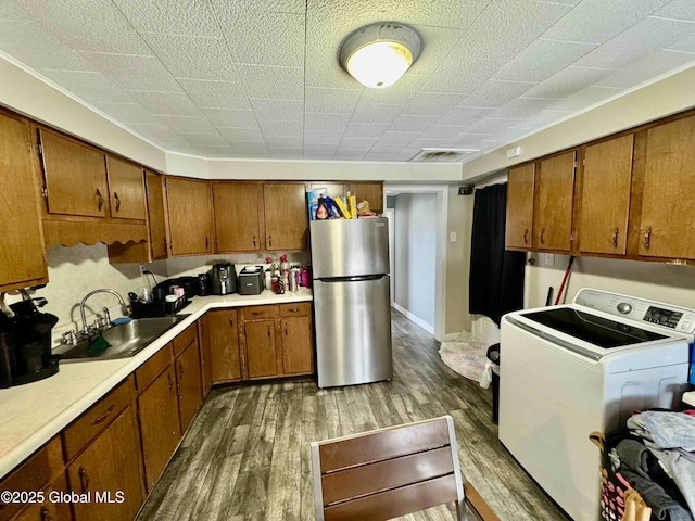 kitchen featuring washer / dryer, freestanding refrigerator, brown cabinetry, and a sink