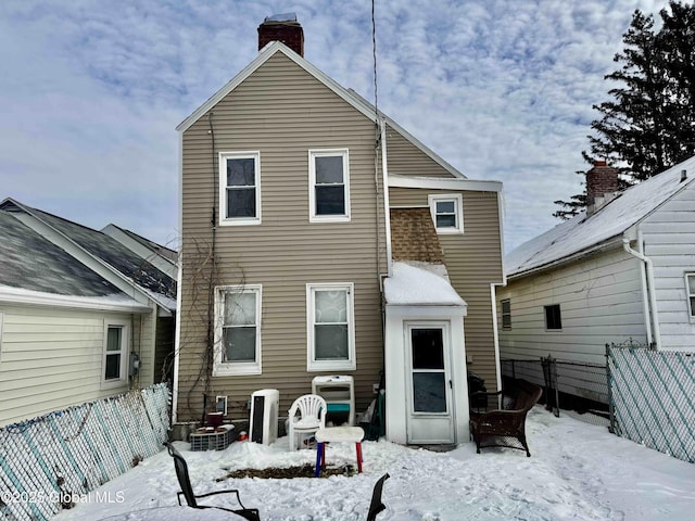 snow covered house featuring a chimney and fence