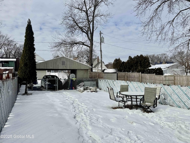 yard covered in snow featuring outdoor dining space, a fenced backyard, and an outbuilding