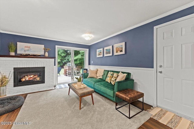 living room with wainscoting, a brick fireplace, wood finished floors, and crown molding