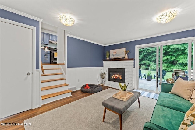 living area with a brick fireplace, wood finished floors, visible vents, and crown molding