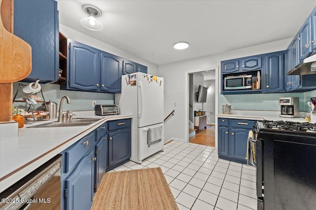 kitchen featuring light tile patterned floors, under cabinet range hood, stainless steel appliances, a sink, and blue cabinetry