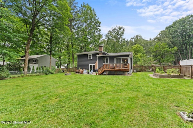 back of property with a deck, an outdoor fire pit, a fenced backyard, a garden, and a yard