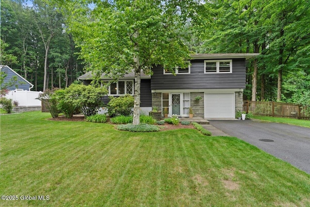 split level home featuring aphalt driveway, an attached garage, fence, stone siding, and a front yard