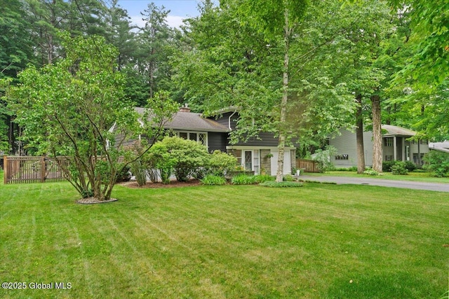 view of front of property featuring driveway, a chimney, fence, and a front yard