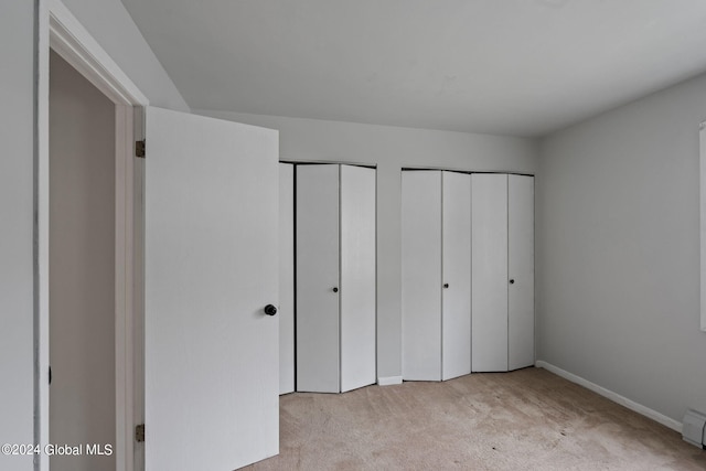 unfurnished bedroom featuring carpet floors, a baseboard heating unit, baseboards, and two closets