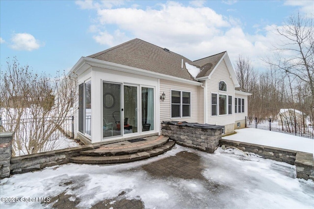 snow covered property with a patio area, fence, and roof with shingles