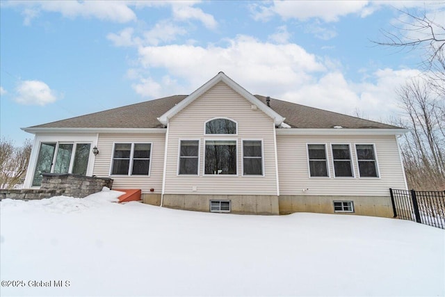 snow covered property featuring a shingled roof and fence