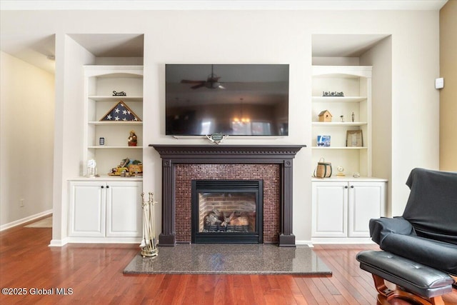 living room featuring built in shelves, baseboards, a tiled fireplace, and wood finished floors