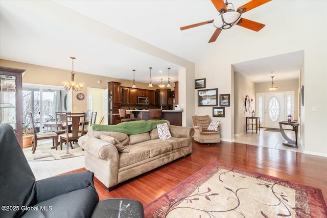 living room with light wood-type flooring, baseboards, vaulted ceiling, and ceiling fan with notable chandelier