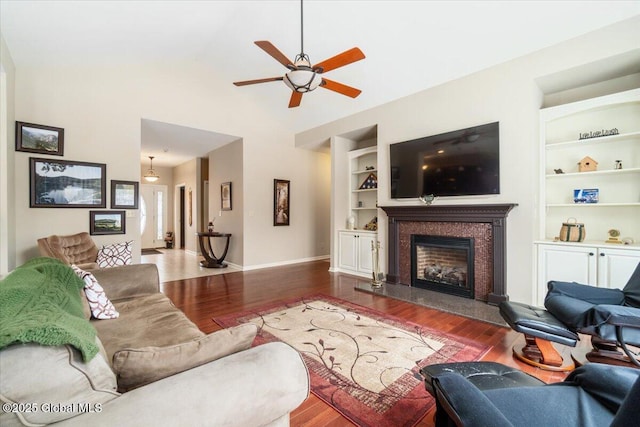 living room with built in shelves, vaulted ceiling, wood finished floors, a tile fireplace, and baseboards