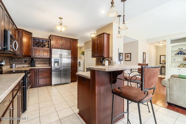 kitchen featuring stainless steel appliances, washer / dryer, a breakfast bar area, and light tile patterned floors