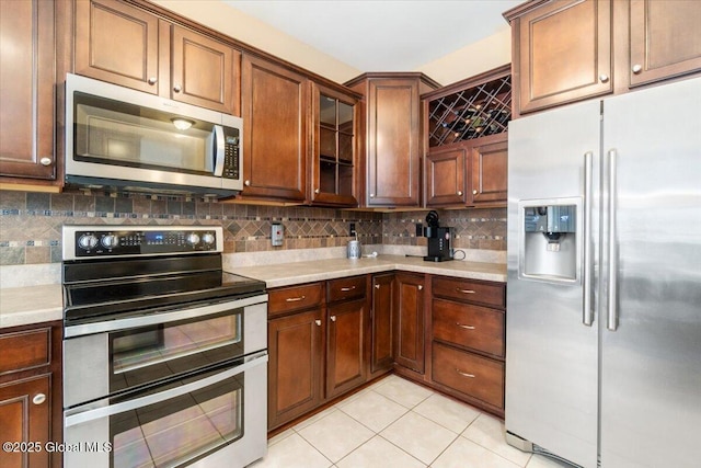 kitchen with light tile patterned flooring, light countertops, appliances with stainless steel finishes, decorative backsplash, and glass insert cabinets