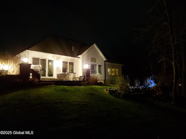 back of house at night featuring a yard