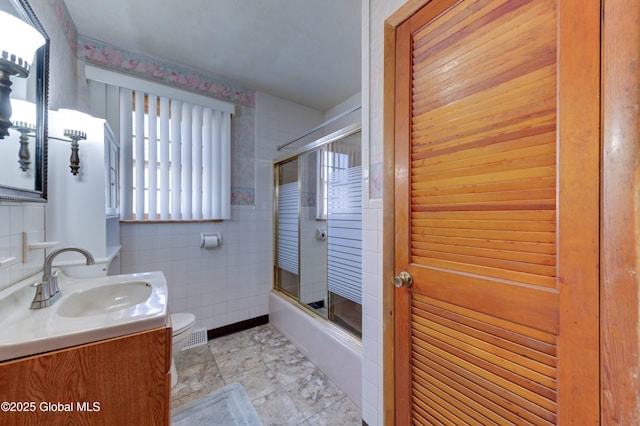 bathroom with tile walls, toilet, enclosed tub / shower combo, and vanity