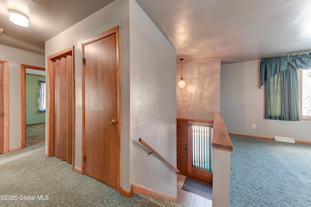 hall with an upstairs landing, carpet flooring, and baseboards