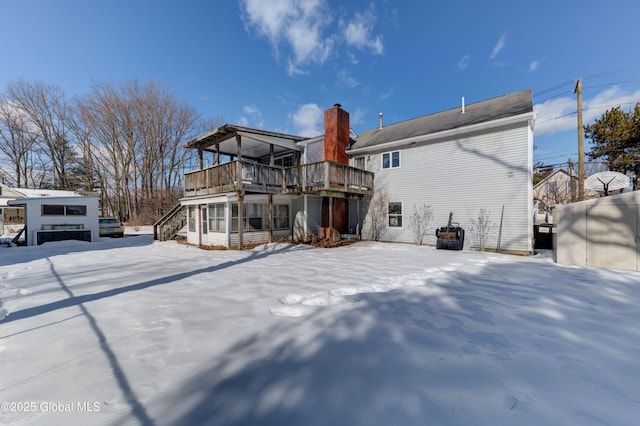snow covered property with a wooden deck and a chimney