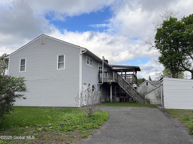 view of side of home featuring stairs, a deck, a chimney, and driveway