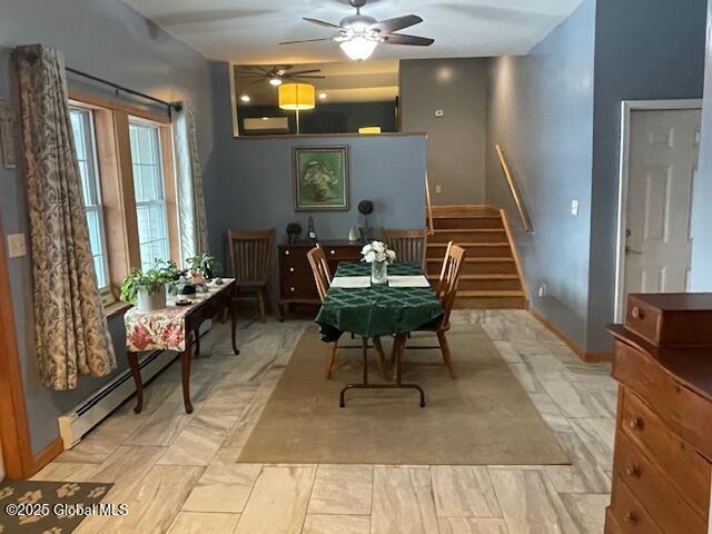 dining space featuring stairs, a baseboard heating unit, a ceiling fan, and baseboards