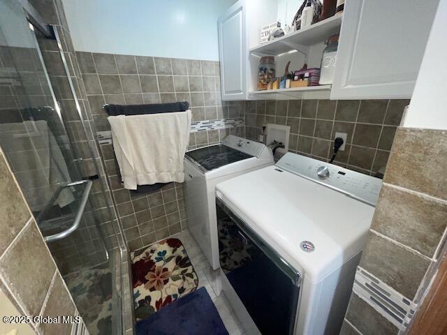 laundry area with separate washer and dryer, cabinet space, and tile walls