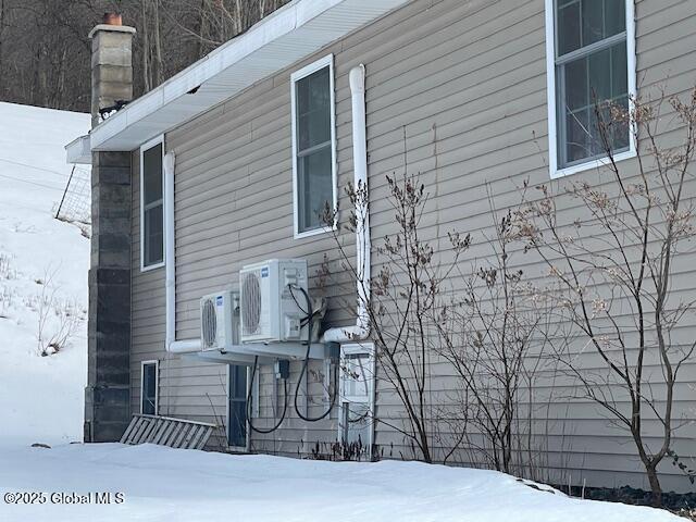 snow covered property with ac unit and a chimney