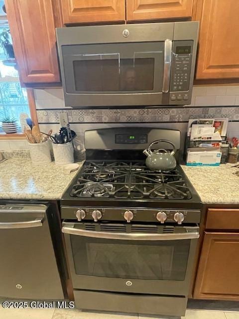 kitchen featuring appliances with stainless steel finishes, backsplash, and light stone countertops