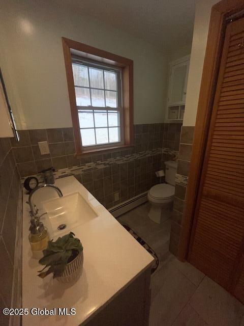 bathroom featuring wainscoting, toilet, a baseboard radiator, tile patterned floors, and tile walls