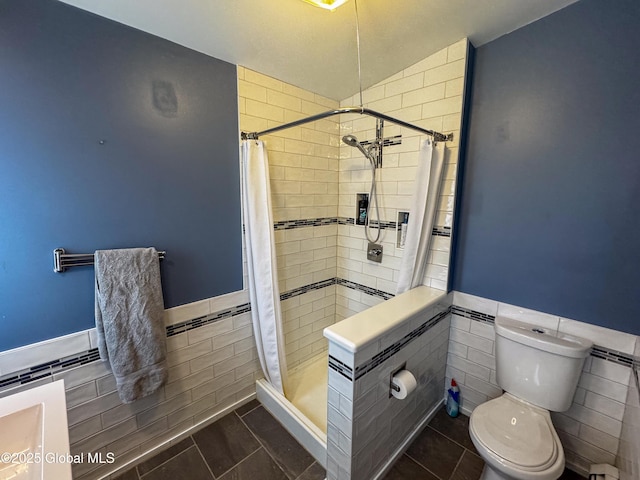 full bathroom with tile patterned flooring, toilet, a wainscoted wall, tile walls, and a shower stall