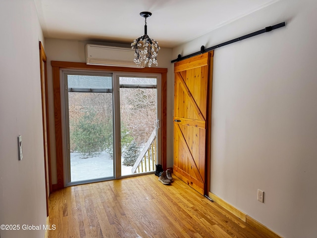 interior space featuring a barn door, a wall unit AC, baseboards, light wood finished floors, and an inviting chandelier