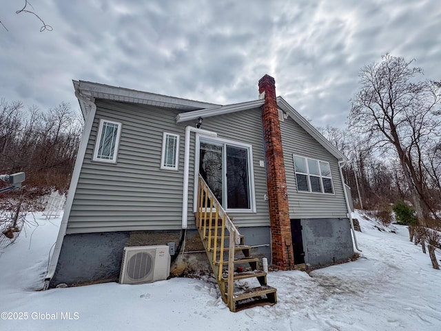 snow covered property with entry steps, ac unit, and a chimney