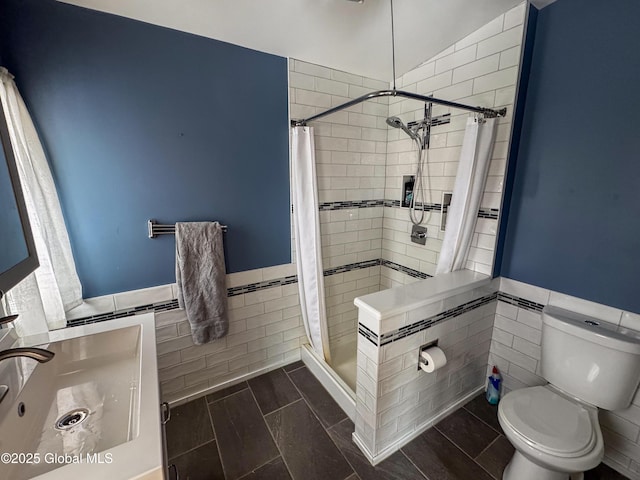 bathroom with toilet, a stall shower, wainscoting, and tile walls