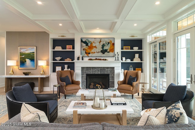 living area with built in shelves, beam ceiling, a warm lit fireplace, wood finished floors, and coffered ceiling