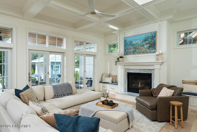 living room with a high end fireplace, beamed ceiling, light wood-style flooring, french doors, and coffered ceiling