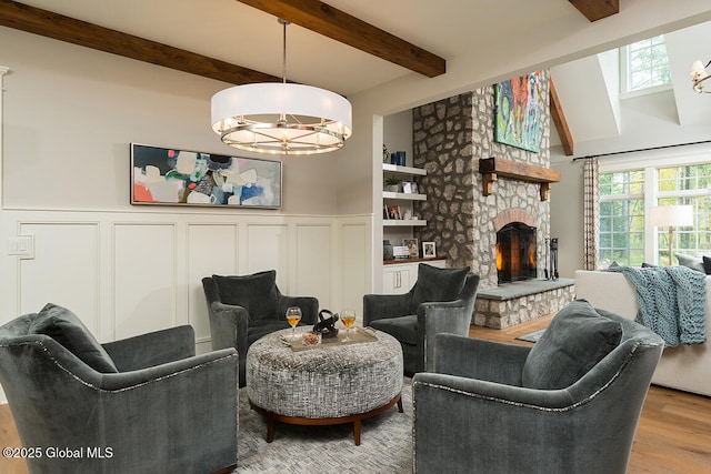 living area featuring wainscoting, a stone fireplace, beamed ceiling, and wood finished floors