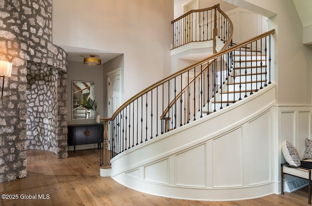 stairway featuring a high ceiling, wood finished floors, wainscoting, and a decorative wall