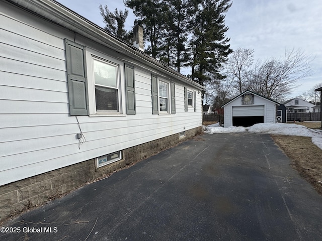 view of side of home with aphalt driveway, a detached garage, fence, an outdoor structure, and a chimney