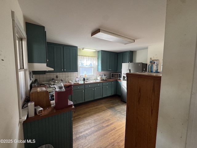 kitchen featuring a sink, decorative backsplash, dark wood-type flooring, stainless steel microwave, and fridge with ice dispenser