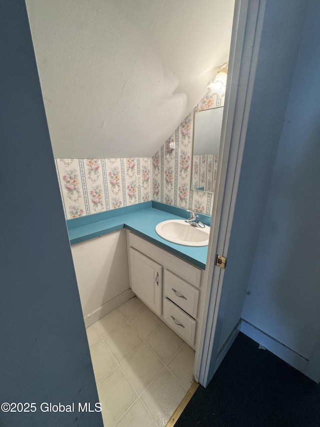 bathroom featuring baseboards, tile patterned flooring, wallpapered walls, lofted ceiling, and vanity