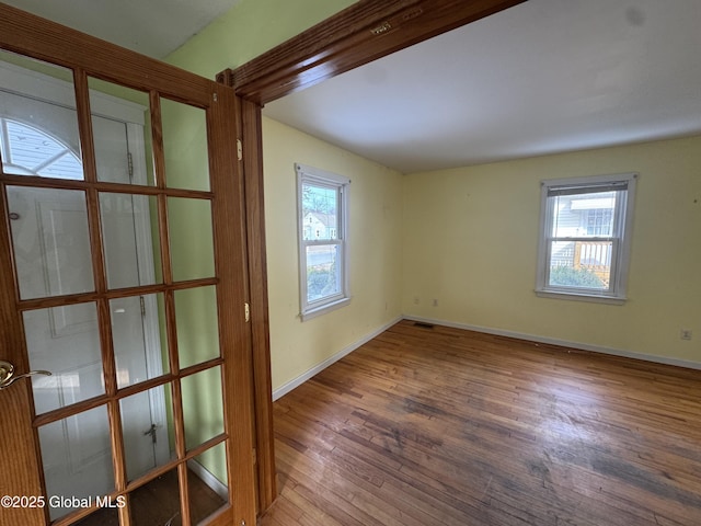 spare room featuring plenty of natural light, visible vents, baseboards, and hardwood / wood-style flooring